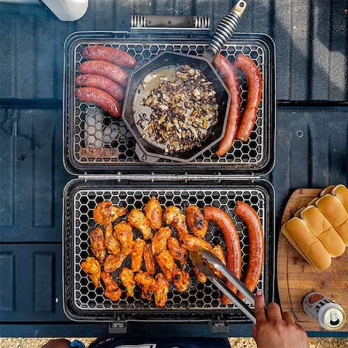 Grilling sausages, wings, onions with buns and drink nearby.